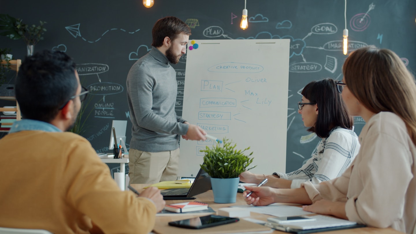 Man presenting creative product strategy on whiteboard to colleagues.