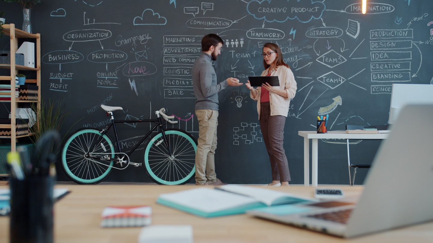 Two professionals discussing a business plan with diagrams on a chalkboard.